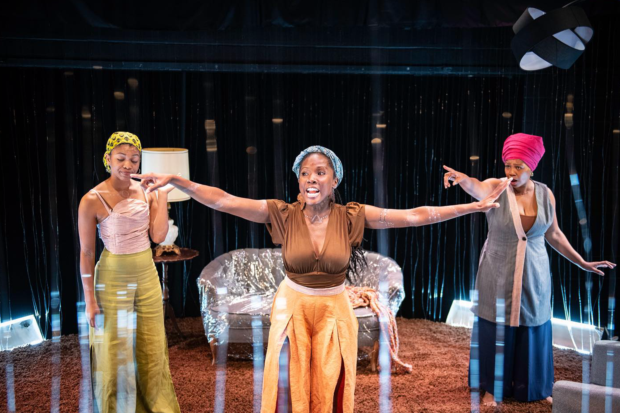 Three Black women face the audience on a theater stage